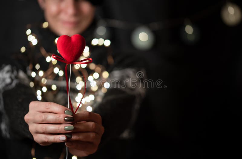 La ragazza tiene il cuore rosso a disposizione su un fondo del bokeh immagini stock La ragazza tiene il cuore rosso a disposizione su un fondo del bokeh immagini stock