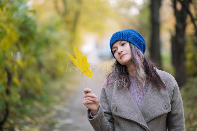 La ragazza in un cappotto ed in un cappello blu su un fondo degli alberi e delle foglie di acero di autunno immagini stock La ragazza in un cappotto ed in un cappello blu su un fondo degli alberi e delle foglie di acero di autunno immagini stock