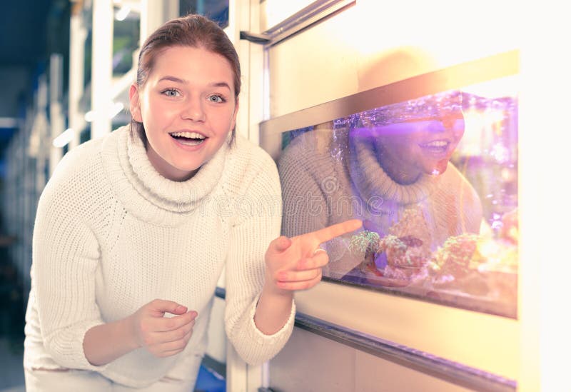 La ragazza vicino al grande acquario sta indicando il modello interessante di aquar immagine stock La ragazza vicino al grande acquario sta indicando il modello interessante di aquar immagine stock