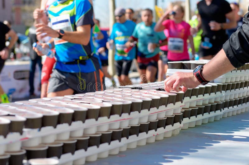 La raza corriente del maratón, corredores en el camino, las bebidas isotónicas en el refresco señala