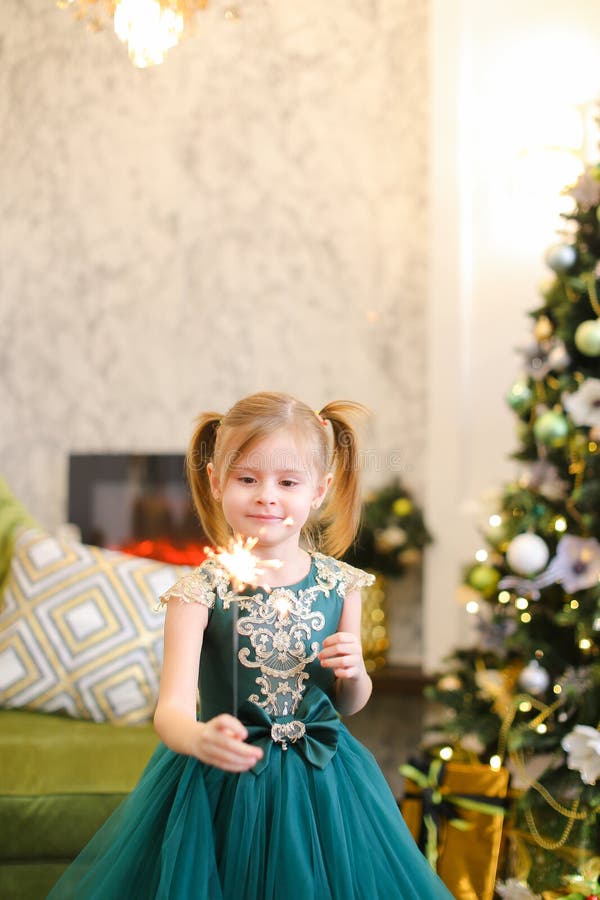 La robe de port et la position de petite gentille fille avec des lumières de Bengale s'approchent de l'arbre de Noël image stock La robe de port et la position de petite gentille fille avec des lumières de Bengale s'approchent de l'arbre de Noël image stock