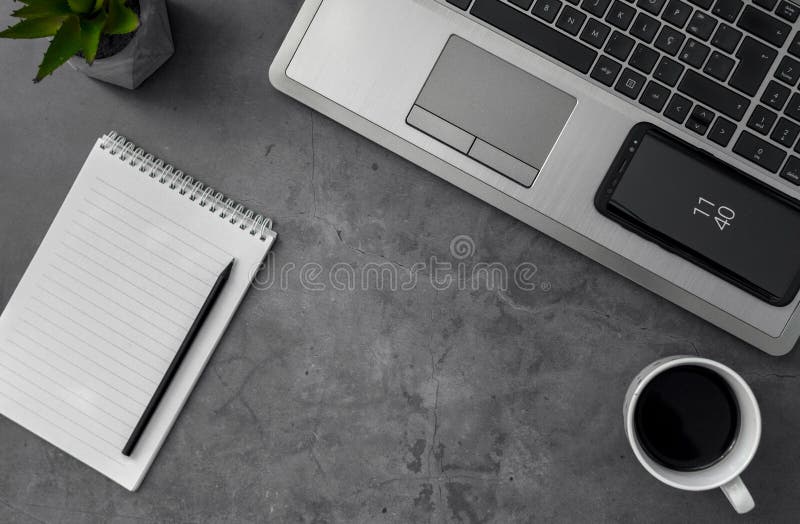 La scala di grigi a vista superiore ha sparato di un caffè e di un notebook del cellulare del computer portatile su una tabella fotografia stock
