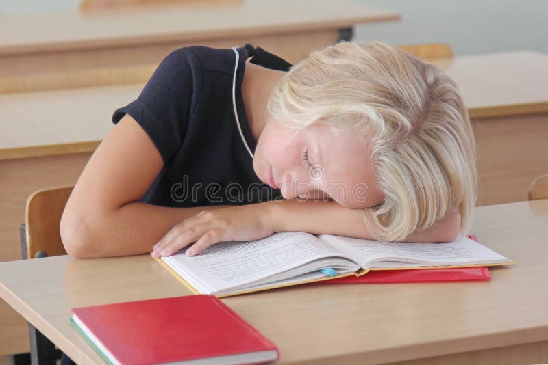 La scolara stanca del bambino dorme durante la lezione allo scrittorio in un'aula fotografia stock libera da diritti La scolara stanca del bambino dorme durante la lezione allo scrittorio in un'aula fotografia stock libera da diritti