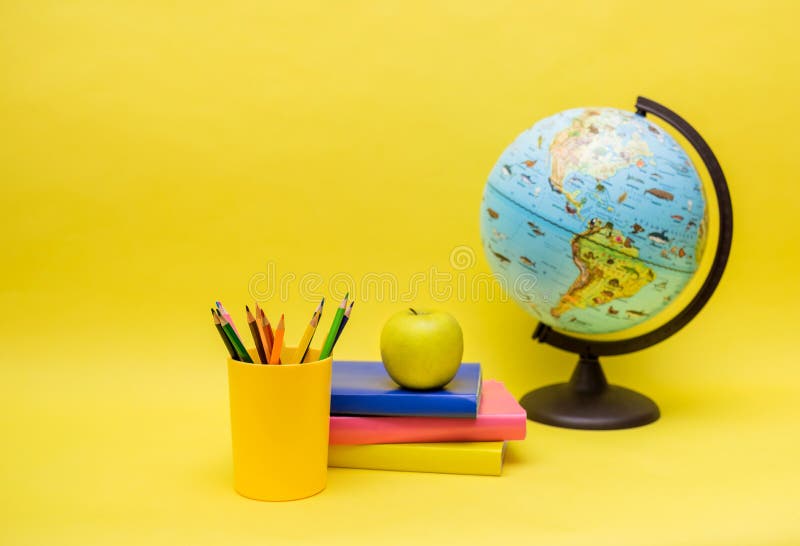 school supplies globe, books, pencils and Apple on a yellow isolated background with a copy of the space. school supplies globe, books, pencils and Apple on a yellow isolated background with a copy of the space