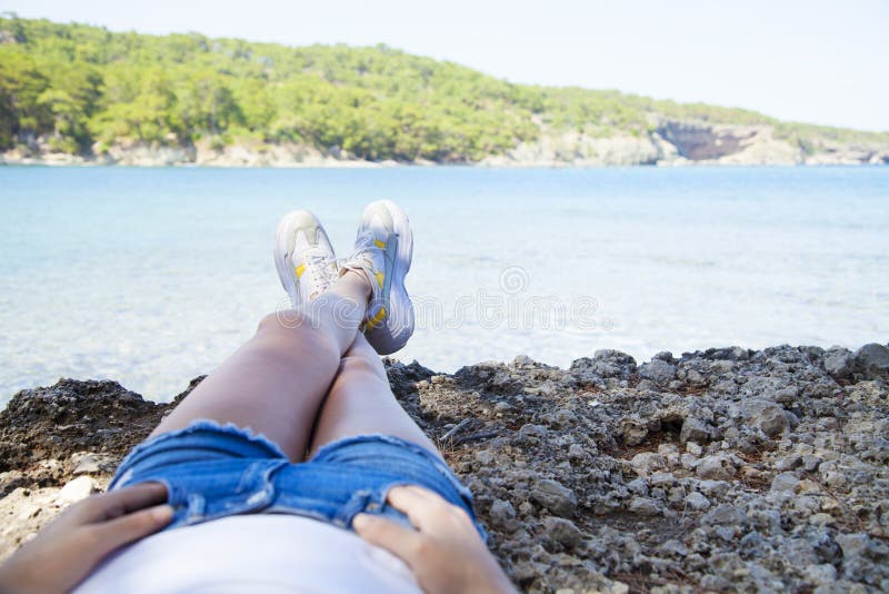 La seduta felice della giovane donna, gode della vita sulla spiaggia in mare fotografia stock La seduta felice della giovane donna, gode della vita sulla spiaggia in mare fotografia stock