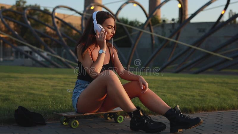 La sentada joven de la mujer del skater y pone los auriculares