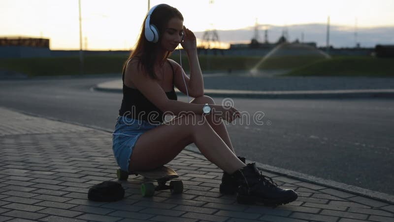 La sentada joven de la mujer del skater y pone los auriculares