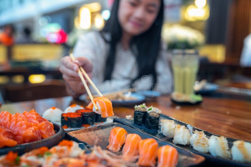 La señora asiática come un sashimi y un sushi de color salmón de los pescados en restaurante japonés