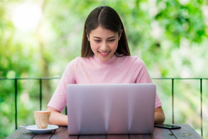 La señora asiática que trabaja con el cuaderno del ordenador y bebe un café fotos de archivo libres de regalías La señora asiática que trabaja con el cuaderno del ordenador y bebe un café fotos de archivo libres de regalías