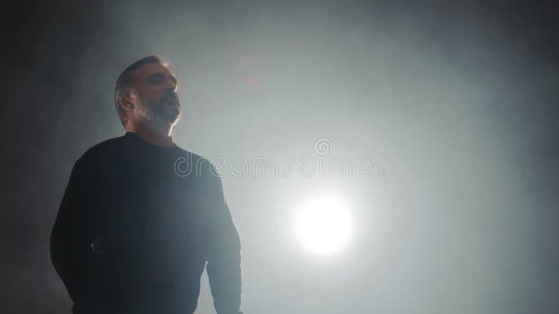 La silhouette d'un chanteur d'opéra chantant sur scène assis dans une chaise est rétroéclairée et la fumée légère. banque de vidéos