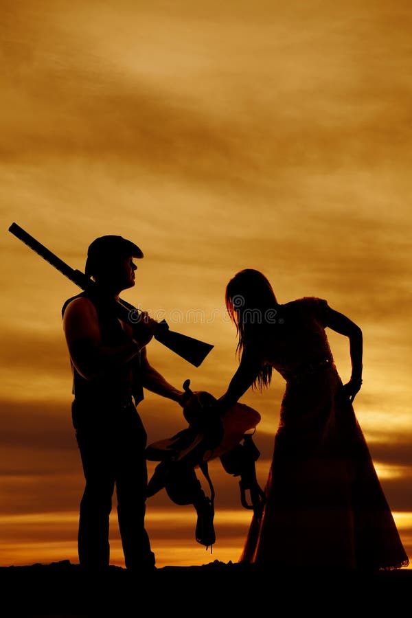 La silhouette des couples de cowboy tiennent la selle et l'arme à feu photo stock La silhouette des couples de cowboy tiennent la selle et l'arme à feu photo stock