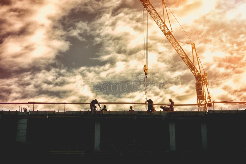 La silhouette des travailleurs sur le dessus du site de construction de bâtiments avec la grue et la lumière du soleil de coucher photos stock La silhouette des travailleurs sur le dessus du site de construction de bâtiments avec la grue et la lumière du soleil de coucher photos stock