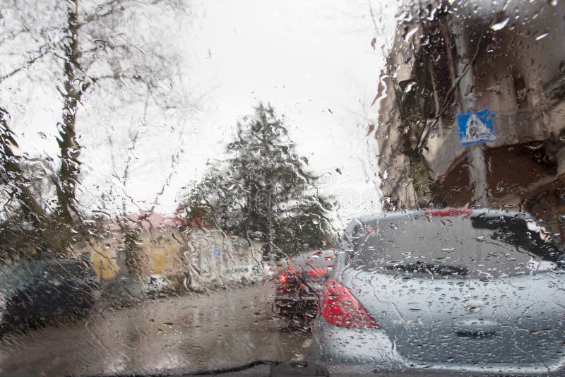 La silueta borrosa del coche vista a través del agua cae en el parabrisas del coche Días lluviosos imagen de archivo La silueta borrosa del coche vista a través del agua cae en el parabrisas del coche Días lluviosos imagen de archivo