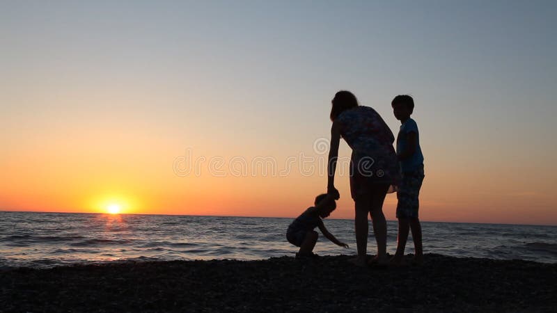 La silueta de la mamá y el hijo en la puesta del sol varan el océano del mar