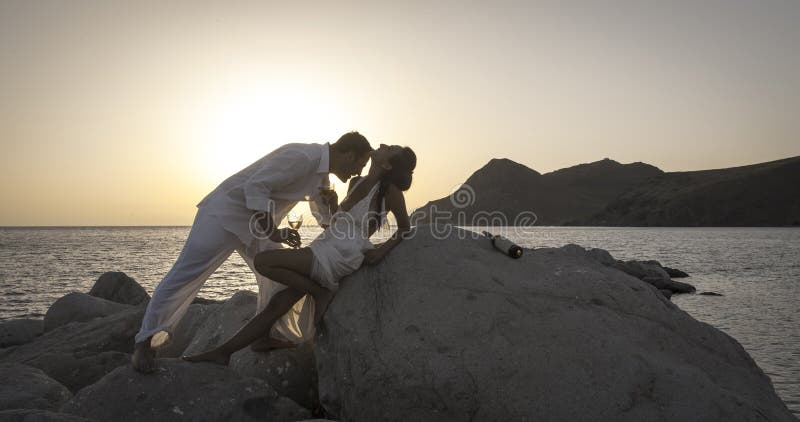 La silueta de los pares felices jovenes que se divierten en la playa oscila en la salida del sol imagen de archivo La silueta de los pares felices jovenes que se divierten en la playa oscila en la salida del sol imagen de archivo