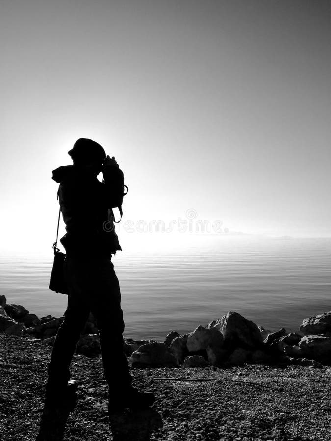 La silueta del hombre del fotógrafo toma una foto en la orilla del lago en la puesta del sol imagen de archivo La silueta del hombre del fotógrafo toma una foto en la orilla del lago en la puesta del sol imagen de archivo