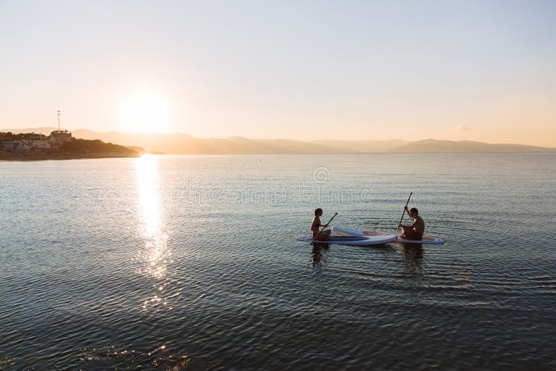 Silhouette of male and female in yoga pose on sup surf swimming at the ocean. Concept lifestyle, sport, love. Silhouette of male and female in yoga pose on sup surf swimming at the ocean. Concept lifestyle, sport, love.