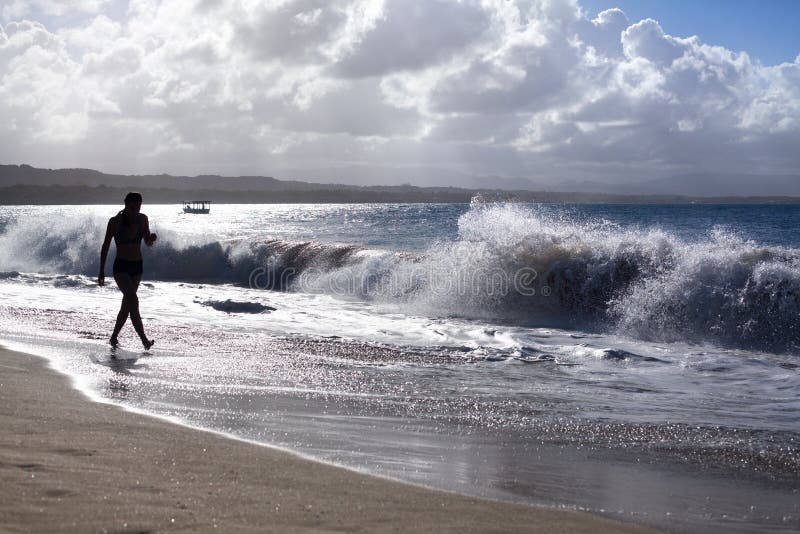 La siluetta della ragazza che cammina lungo la spiaggia con le onde ed acqua spruzza in vacanza, mare blu, onde espone al sole il fotografie stock libere da diritti La siluetta della ragazza che cammina lungo la spiaggia con le onde ed acqua spruzza in vacanza, mare blu, onde espone al sole il fotografie stock libere da diritti