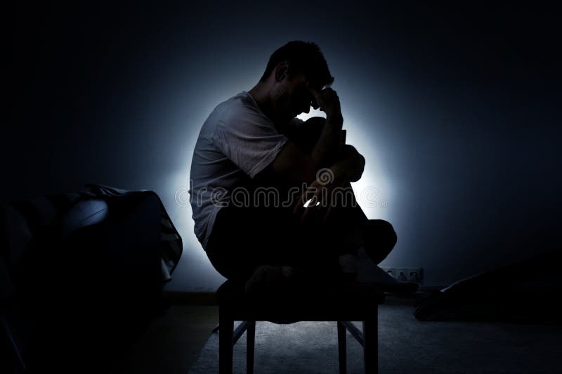 La siluetta triste di un uomo nella depressione che si siede su una sedia con la sua testa giù, pensa a vita