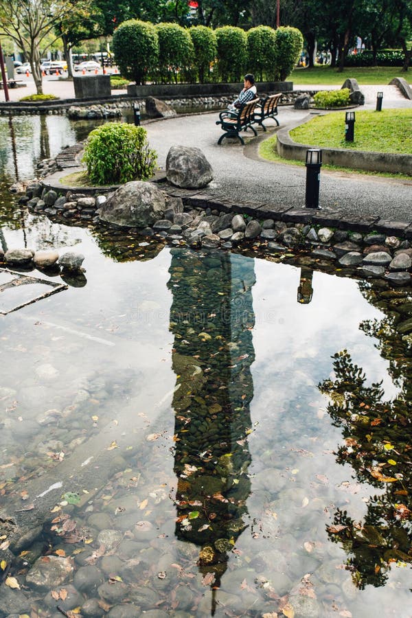 La sombra del rascacielos de Taipei 101 reflejó en la piscina en el parque con un hombre que se sentaba en la silla fotografía de archivo libre de regalías La sombra del rascacielos de Taipei 101 reflejó en la piscina en el parque con un hombre que se sentaba en la silla fotografía de archivo libre de regalías