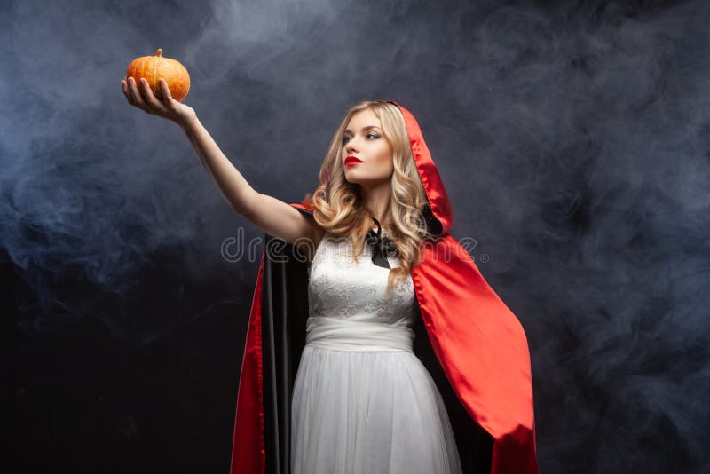 La sorcière d'Halloween avec une citrouille sculptée et une fumée magique Belle jeune femme surprise en chapeau de sorcière et co photo stock La sorcière d'Halloween avec une citrouille sculptée et une fumée magique Belle jeune femme surprise en chapeau de sorcière et co photo stock