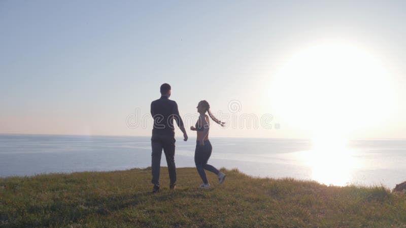 La sportive heureuse saute sur masculin et des mouvements giratoires sur la pelouse verte sur la falaise de rivière en soleil lum