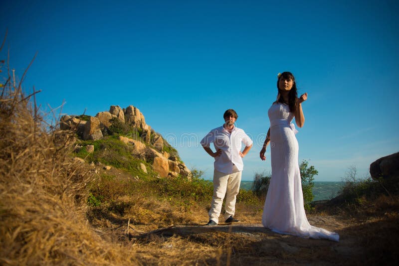 La sposa e lo sposo stanno sui precedenti delle montagne e del cielo fotografia stock La sposa e lo sposo stanno sui precedenti delle montagne e del cielo fotografia stock