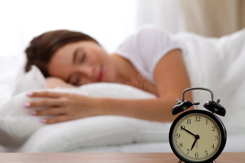 La sveglia che sta sul comodino già ha suonato il primo mattino per svegliare la donna a letto che dorme nel fondo fotografia stock libera da diritti La sveglia che sta sul comodino già ha suonato il primo mattino per svegliare la donna a letto che dorme nel fondo fotografia stock libera da diritti