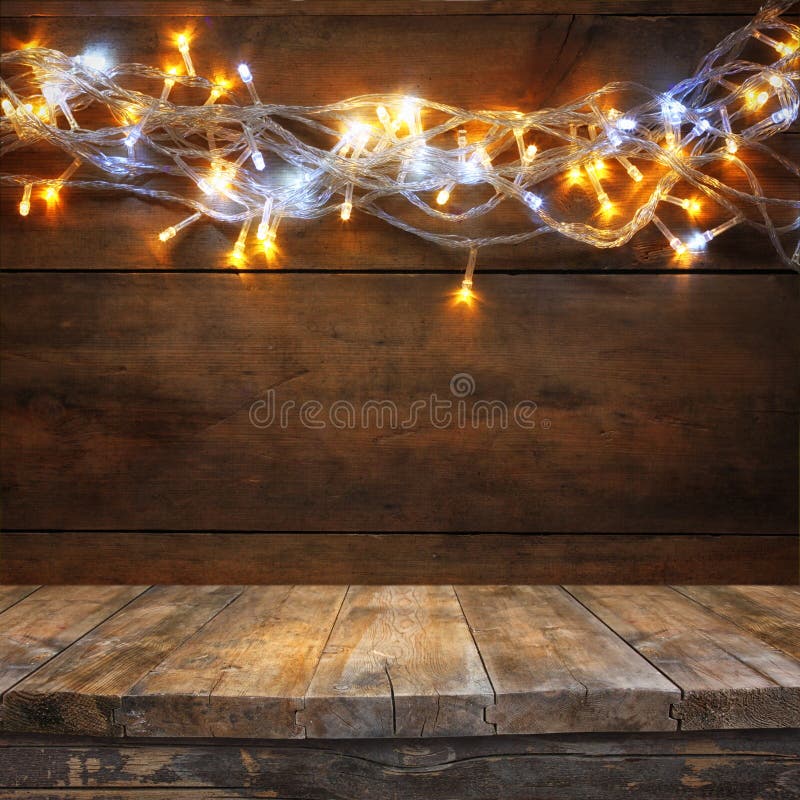 La table en bois de conseil devant la guirlande chaude d'or de Noël s'allume sur le fond rustique en bois Image filtrée Foyer sél photographie stock La table en bois de conseil devant la guirlande chaude d'or de Noël s'allume sur le fond rustique en bois Image filtrée Foyer sél photographie stock