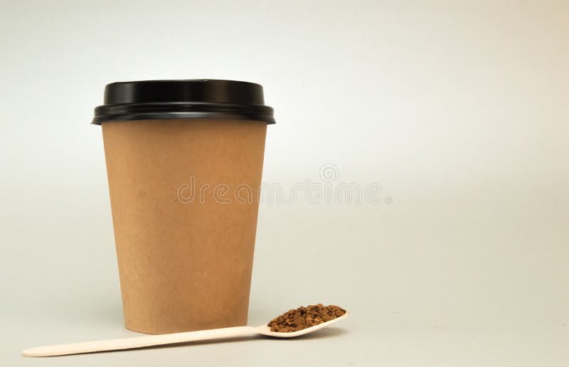 La taza de papel para el café con una tapa negra en un fondo ligero, al lado de ella es una cuchara de madera con café imágenes de archivo libres de regalías La taza de papel para el café con una tapa negra en un fondo ligero, al lado de ella es una cuchara de madera con café imágenes de archivo libres de regalías