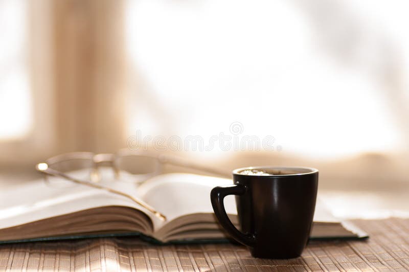 La taza de vidrios del café descansa sobre el libro abierto contra fotos de archivo La taza de vidrios del café descansa sobre el libro abierto contra fotos de archivo