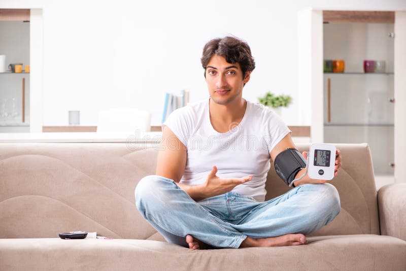 La tension artérielle de mesure de jeune homme à la maison photos stock La tension artérielle de mesure de jeune homme à la maison photos stock