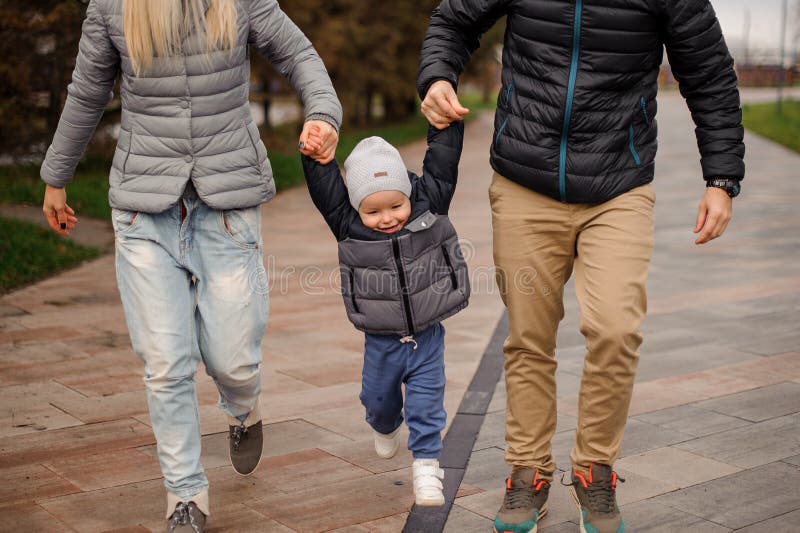 La tenuta sveglia del ragazzino parents le mani ed il salto immagine stock libera da diritti La tenuta sveglia del ragazzino parents le mani ed il salto immagine stock libera da diritti