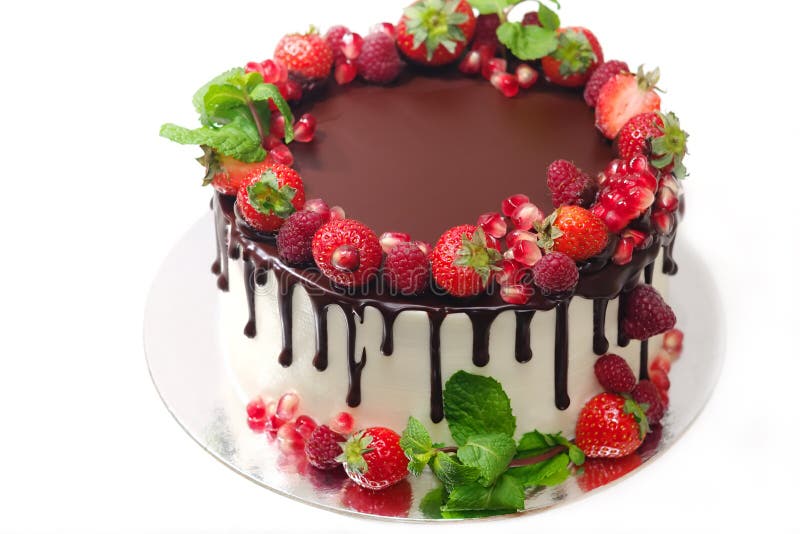 La torta cubierta con las bayas de las hojas de menta de la granada de la fresa de la frambuesa doused con el chocolate en un fon fotografía de archivo La torta cubierta con las bayas de las hojas de menta de la granada de la fresa de la frambuesa doused con el chocolate en un fon fotografía de archivo