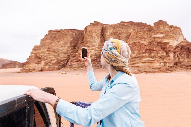 La touriste de femme tire la vidéo ou la photo au téléphone portable du désert jordanien photo stock La touriste de femme tire la vidéo ou la photo au téléphone portable du désert jordanien photo stock