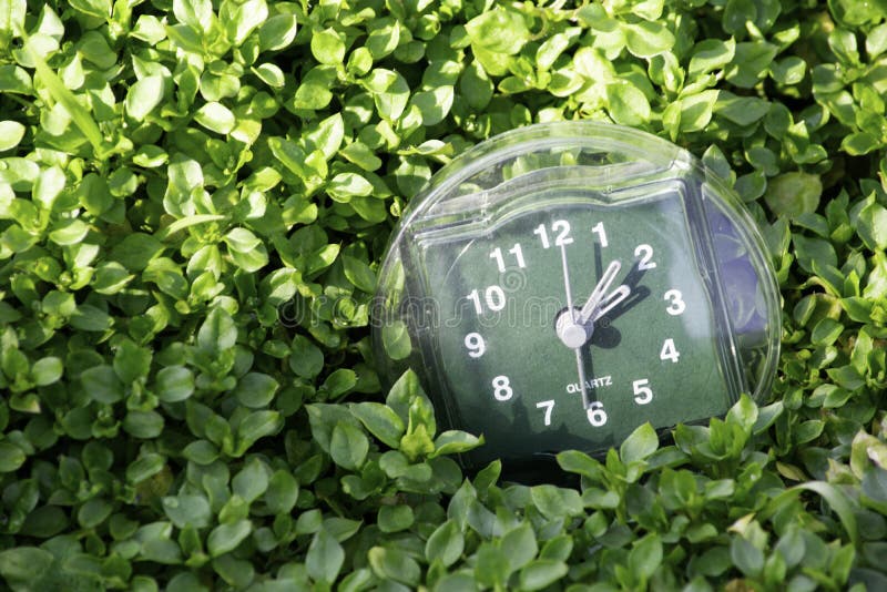 La transición al tiempo de verano, la llegada de la primavera, el reloj en el fondo de la hierba verde clara de la primavera con fotos de archivo libres de regalías La transición al tiempo de verano, la llegada de la primavera, el reloj en el fondo de la hierba verde clara de la primavera con fotos de archivo libres de regalías