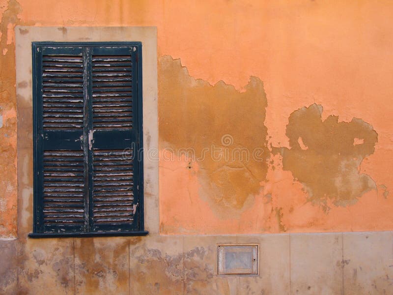 La ventana vieja con los obturadores de madera cerrados pintados verdes en una naranja coloreada ocre mediterránea anaranjada se fotos de archivo libres de regalías La ventana vieja con los obturadores de madera cerrados pintados verdes en una naranja coloreada ocre mediterránea anaranjada se fotos de archivo libres de regalías