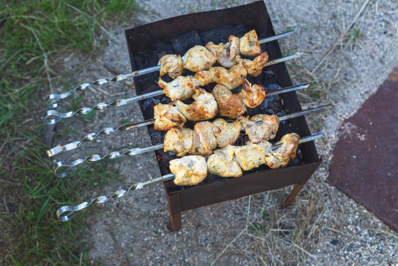 Skewered meat is fried on charcoal on a grill or brazier, top view. Picnic, evening with friends and family, cooking over an open fire in the front or backyard. Charcoal grill. Skewered meat is fried on charcoal on a grill or brazier, top view. Picnic, evening with friends and family, cooking over an open fire in the front or backyard. Charcoal grill.