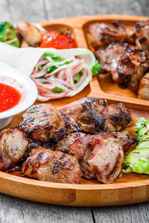 La viande et les légumes grillés délicieux assortis avec de la salade et le BBQ frais sauce sur la planche à découper sur le fond photos stock La viande et les légumes grillés délicieux assortis avec de la salade et le BBQ frais sauce sur la planche à découper sur le fond photos stock
