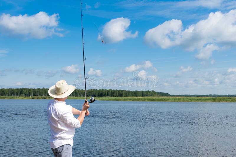 La visión trasera, un hombre lanza una caña de pescar en el río en tiempo soleado fotos de archivo La visión trasera, un hombre lanza una caña de pescar en el río en tiempo soleado fotos de archivo