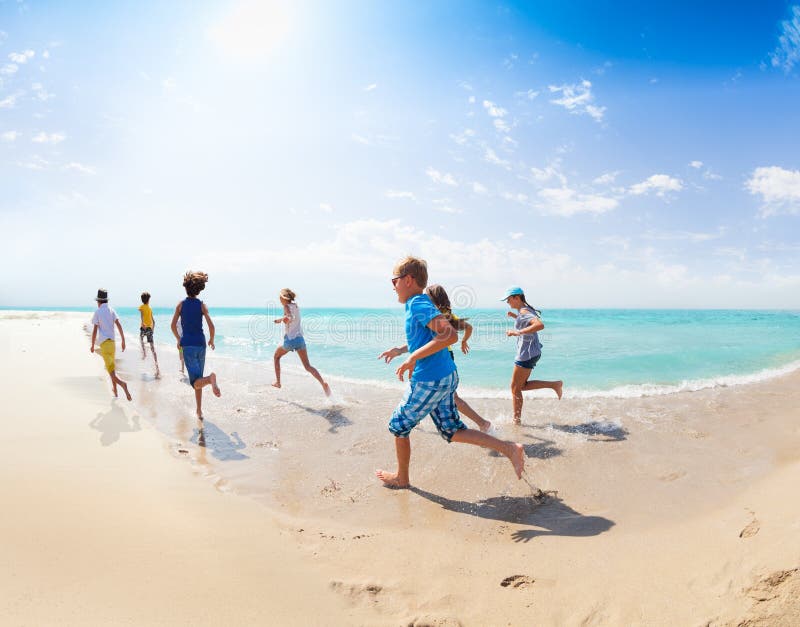 La vista da dietro dei bambini funziona sulla spiaggia del mare immagine stock libera da diritti La vista da dietro dei bambini funziona sulla spiaggia del mare immagine stock libera da diritti