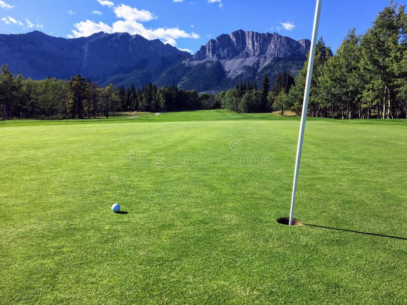 La vista di una foto straordinaria con una pallina da golf su un verde vicino al buco con le montagne e la foresta sullo sfondo immagini stock La vista di una foto straordinaria con una pallina da golf su un verde vicino al buco con le montagne e la foresta sullo sfondo immagini stock