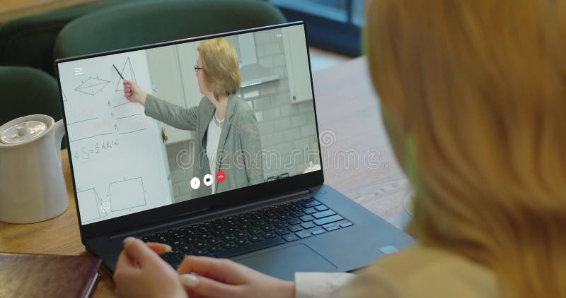La vista posterior de la mujer caucásica con el pelo rojo está sentado en el escritorio en casa y está teniendo una lección en lín almacen de metraje de vídeo