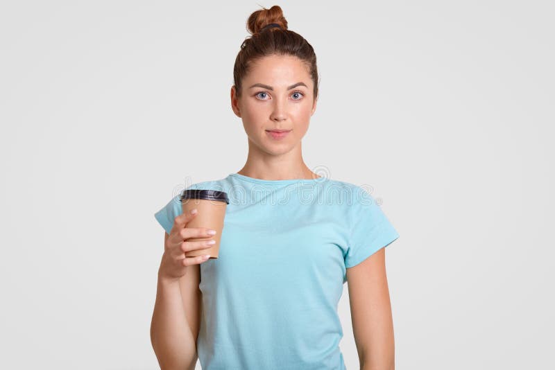 La vita sul ritratto della donna di sguardo piacevole con il panino dei capelli, vestito in maglietta blu-chiaro casuale, tiene l fotografia stock La vita sul ritratto della donna di sguardo piacevole con il panino dei capelli, vestito in maglietta blu-chiaro casuale, tiene l fotografia stock