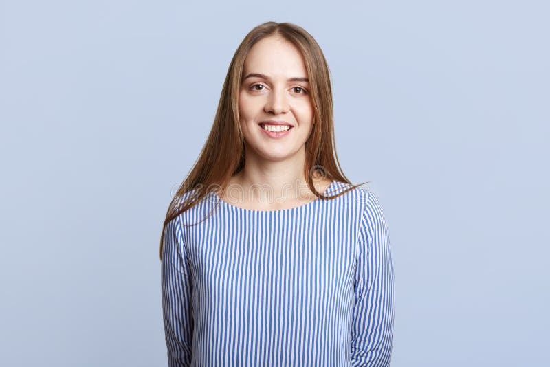 La vita sul ritratto della femmina adorabile con capelli scuri lunghi, vestito in blusa a strisce, esprime le emozioni positive, immagine stock La vita sul ritratto della femmina adorabile con capelli scuri lunghi, vestito in blusa a strisce, esprime le emozioni positive, immagine stock