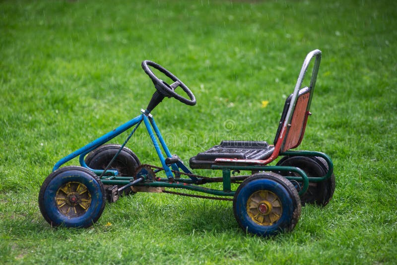 Old children's car, standing on green grass in the rain. Forgotten toys. Old children's car, standing on green grass in the rain. Forgotten toys.