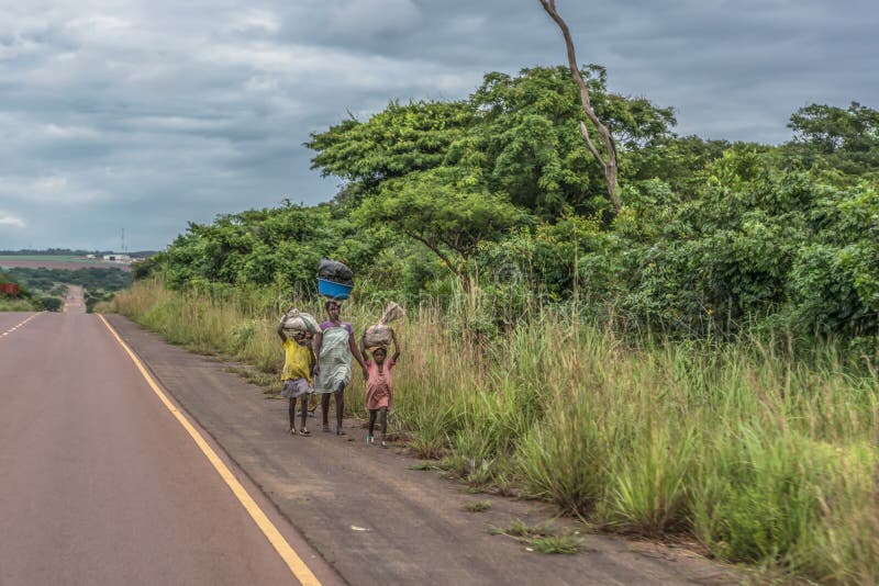 La vue de la femme avec des enfants marche avec la charge principale, le long du bord de la route, paysage tropical comme fond photos libres de droits La vue de la femme avec des enfants marche avec la charge principale, le long du bord de la route, paysage tropical comme fond photos libres de droits