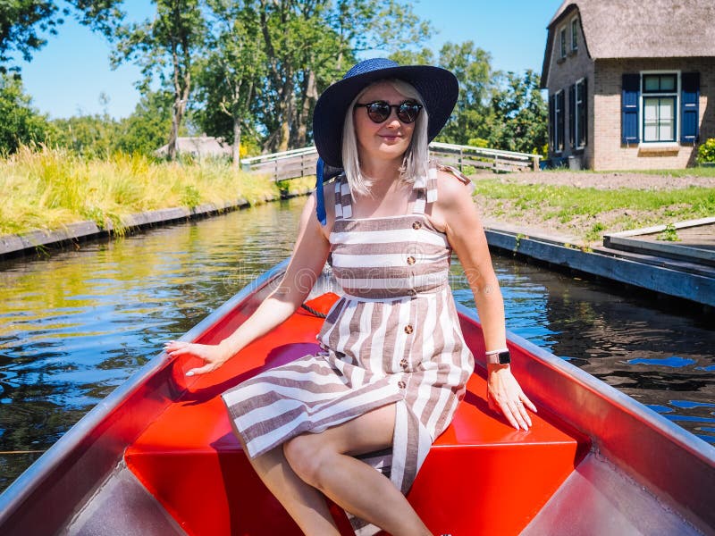 La vue de la fille avec les cheveux blonds et le chapeau bleu se reposent sur un tour de bateau à la rivière dans le village néer photos stock La vue de la fille avec les cheveux blonds et le chapeau bleu se reposent sur un tour de bateau à la rivière dans le village néer photos stock