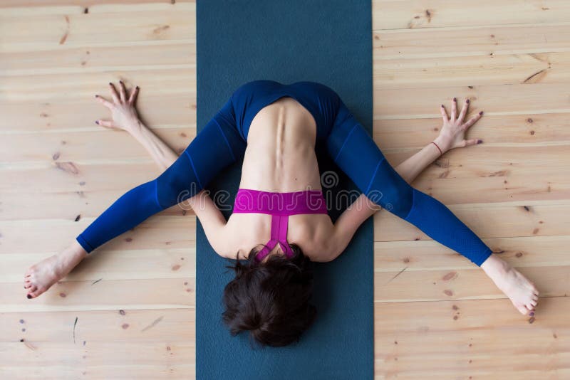 La vue supérieure du yogi féminin faisant la tortue avancée de kurmasana posent sur le tapis à l'intérieur tout en pratiquant le photographie stock La vue supérieure du yogi féminin faisant la tortue avancée de kurmasana posent sur le tapis à l'intérieur tout en pratiquant le photographie stock