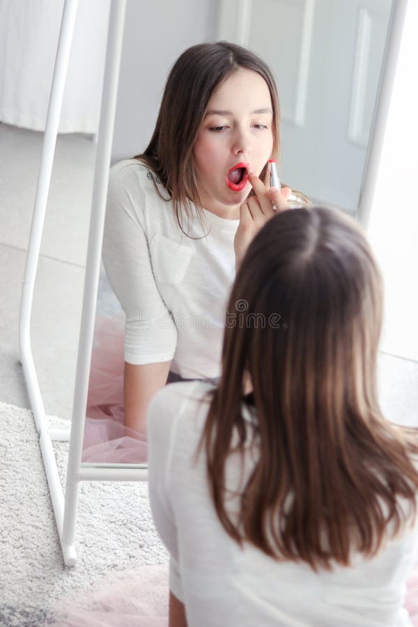 Labbra graziose del rossetto della ragazza della Tween che tengono rossetto rosso che esamina grande specchio fotografie stock libere da diritti Labbra graziose del rossetto della ragazza della Tween che tengono rossetto rosso che esamina grande specchio fotografie stock libere da diritti